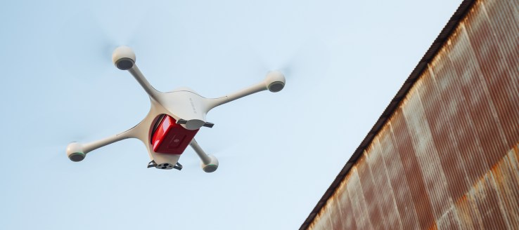 A self-flying, Matternet 2 drone hoists a package near a shipping container.