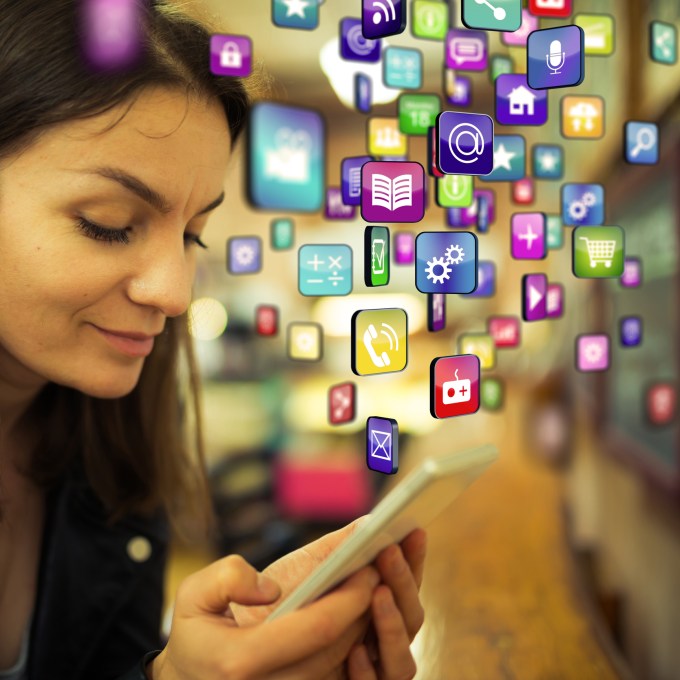 Casual woman inside a cafe downloading or sharing information with a smartphone . A lot of apps, media and other information flying out or into the phone
